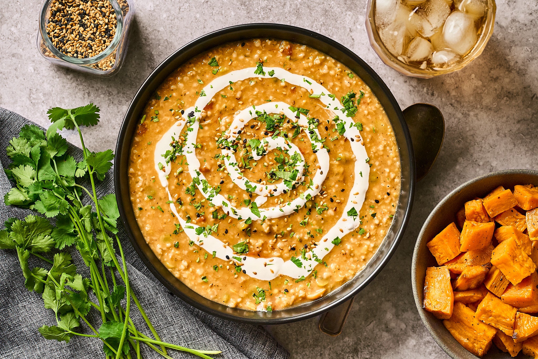 A bowl of no-fuss Sundown Mix stew swirled with yoghurt, with coriander, roasted sweet potato and toasted sesame alongside