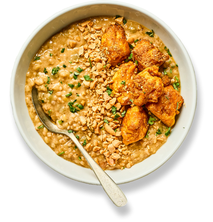 A bowl of one-pot chicken and lentils, topped with crushed peanuts and coriander